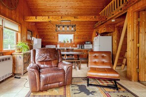 L’intérieur d’une cabane comprend un coin repas, des fauteuils en cuir, une cuisine et un escalier en bois.