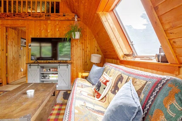 A cozy cabin with a loft bedroom, a dining area, and a TV.