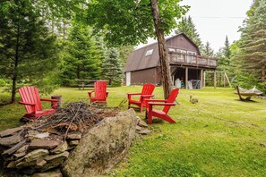 Eine rustikale Holzhütte mit einer Terrasse, umgeben von einem grünen Rasen und Bäumen.