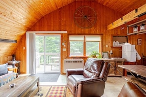Ein Holzblock-Interieur mit Ledersofa, Esstisch und großem Fenster mit Blick auf eine Terrasse.
