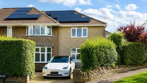 Een woonhuis met twee verdiepingen, voorzien van zonnepanelen op het dak, een witte auto op de oprit en een verzorgde haag.