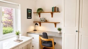 Een studeerkamer met een bureau, stoel, kasten en een raam met uitzicht op groen.