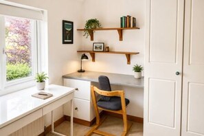 A study with a desk, chair, shelves, and a window with a view of greenery.