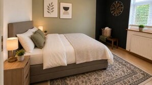 Een slaapkamer met een bed, nachtkastje, lamp, decoratie aan de muur, klok, raam en verwarming.