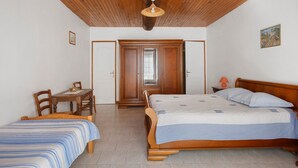 A bedroom with two single beds, a wooden ceiling, a dining table with chairs, and a small table with a lamp.
