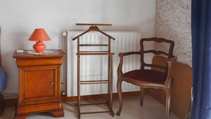 A corner of a room with a radiator, a wooden chair, a wooden dresser, and a lamp.