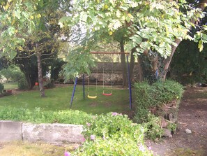 A garden with a swing set, a stone wall, and various plants.