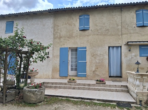 A two-story building with blue shutters, a stone staircase, and potted plants.