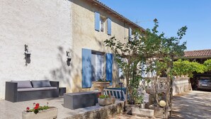 A building with a rustic exterior, outdoor seating area with wicker furniture, and potted plants. - Guest Room "Les Lilas" with Shared Terrace, Communal Garden and Wi-Fi (Antezant-la-Chapelle)