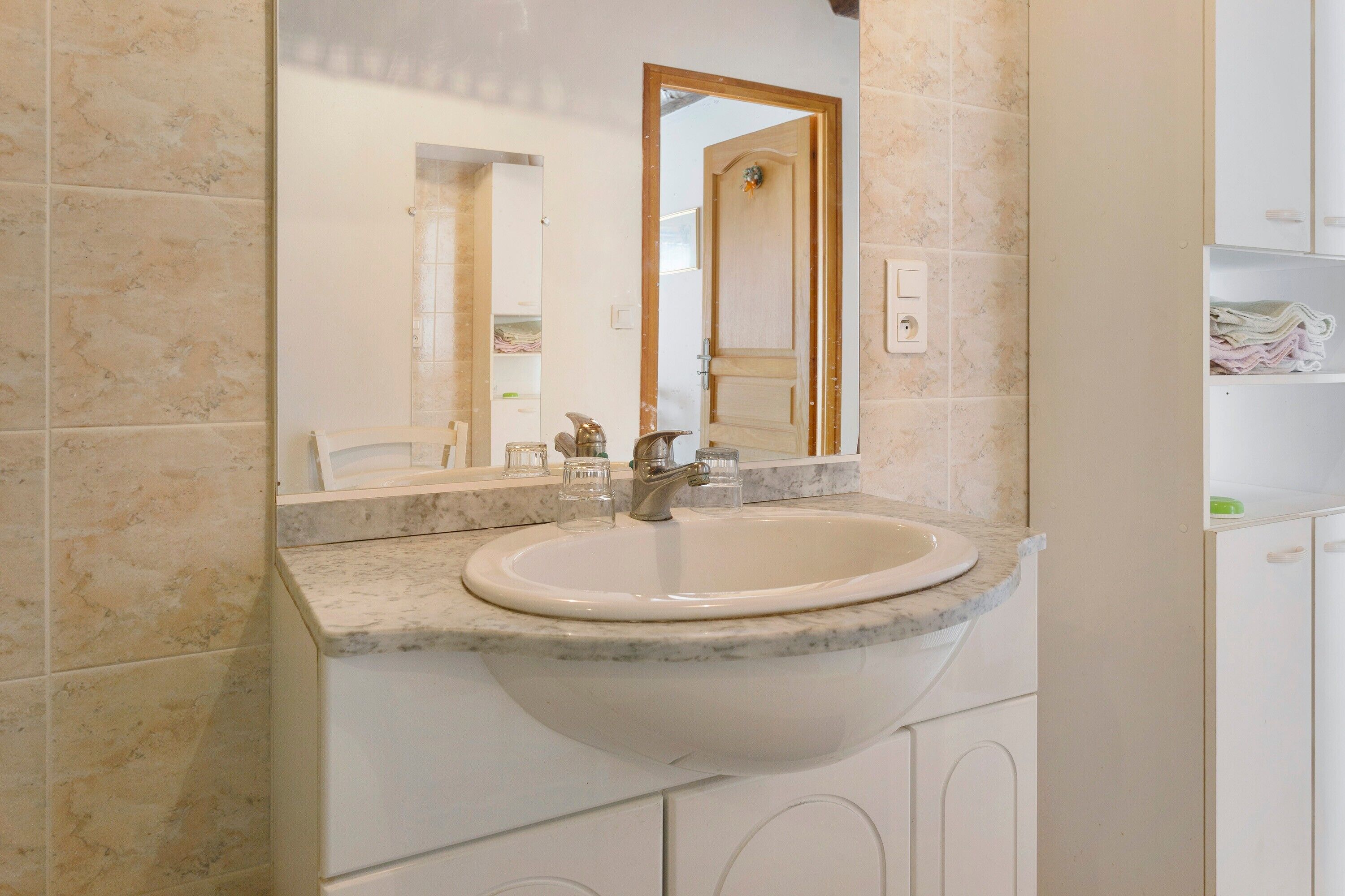 A bathroom with a marble sink, a mirror, and a wooden door.