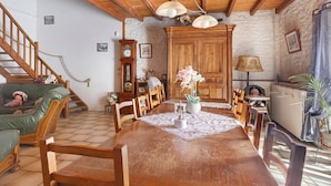 A dining area with a wooden table, chairs, a clock, and a staircase. - Guest Room "Les Lilas" with Shared Terrace, Communal Garden and Wi-Fi (Antezant-la-Chapelle)