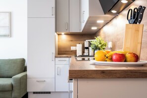 Eine Küche mit einer Holzausziehtafel, einer Kaffeemaschine und einer Obstschale mit Äpfeln und Orangen.