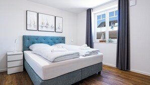 A neatly made bed with white linens, a blue headboard, and a bedside table with a lamp. - Dune anchor 10. balcony. Sauna. central (Grömitz)