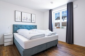 Ein ordentlich bezogenes Bett mit weißen Leinen, einem blauen Kopfteil und einem Nachttisch mit einer Lampe.