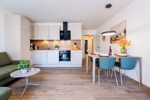 A modern kitchen with white cabinets, a built-in oven, and a dining area with a table set for two. - Dune anchor 10. balcony. Sauna. central (Grömitz)