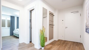 A hotel room with a wooden floor, a bed, a bathroom with a shower, and a hallway with a plant. - Dune anchor 10. balcony. Sauna. central (Grömitz)