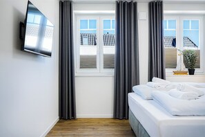 Ein Hotelzimmer mit einem Bett, einem an der Wand befestigten Fernseher und einem Fenster mit Vorhängen.