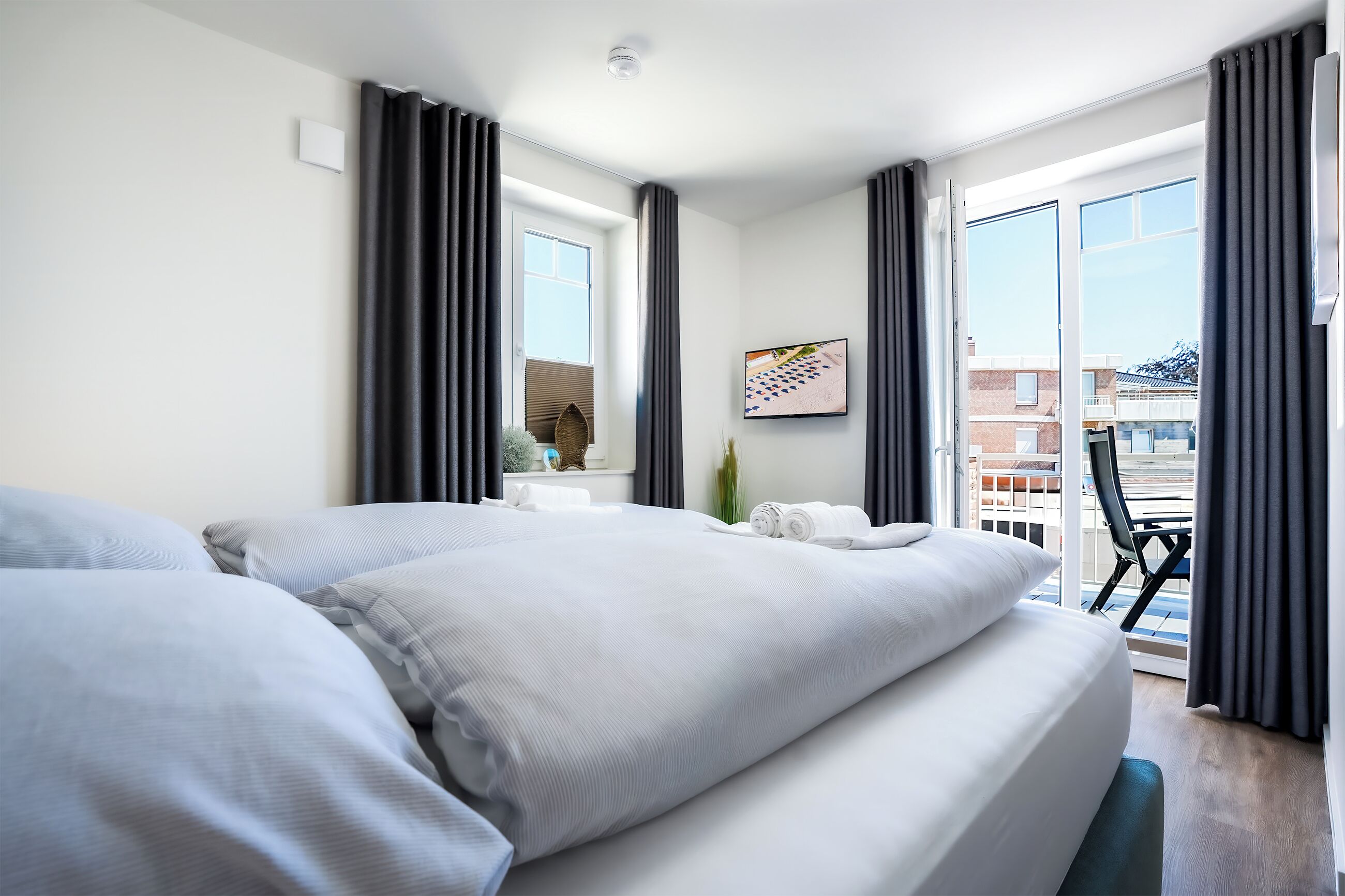 A hotel room with a large bed, a flat-screen TV, and a balcony with a view of buildings.