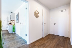 A modern hallway with a wooden floor, white walls, and a door with a circular decorative element. - Dünenanker 12. Infrared cabin. Roof terrace. Central location. (Grömitz)