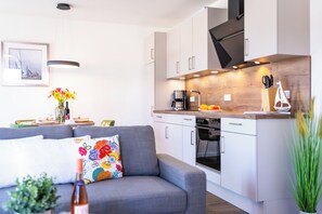 A modern kitchen with white cabinets, a built-in oven, and a coffee maker. - Dünenanker 12. Infrared cabin. Roof terrace. Central location. (Grömitz)