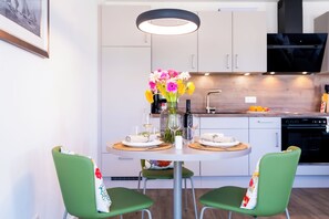 A modern kitchen with white cabinets, a dining table set for two, and a hanging light fixture. - Dünenanker 12. Infrared cabin. Roof terrace. Central location. (Grömitz)