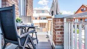 Ein Balkon mit Tisch und Stühlen, einem Blumentopf und Blick auf ein Gebäude mit Ziegeldach.