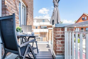 A balcony with a table and chairs, a potted plant, and a view of a building with a tiled roof. - Dünenanker 12. Infrared cabin. Roof terrace. Central location. (Grömitz)