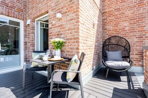 Eine Terrasse mit Tisch für zwei Personen, einem Korbstuhl und einer Backsteinmauer.