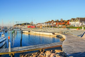 Ein Yachthafen mit vertäuten Booten, einer Holzpromenade und Gebäuden im Hintergrund.