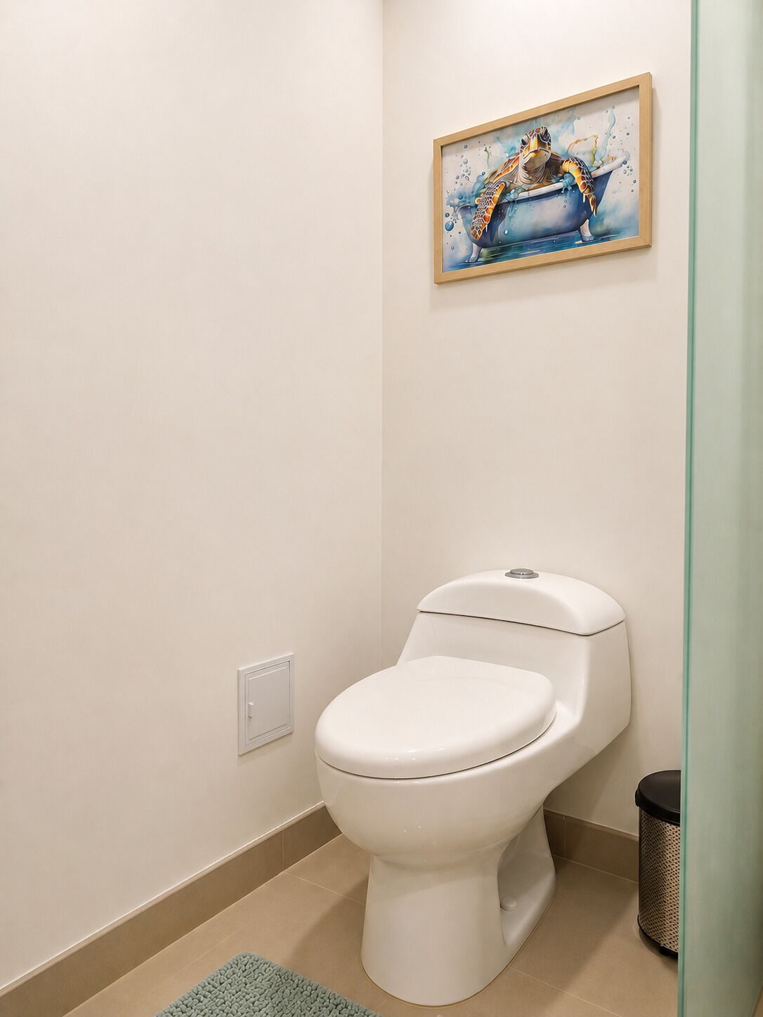 Ein Badezimmer mit einer weißen Toilette, einem gerahmten Gemälde einer Schildkröte und einem Mülleimer.