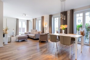 Ein modernes Wohnzimmer mit einer Couch, einem Esstisch mit Stühlen und Blick ins Freie durch große Fenster.