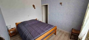Een slaapkamer met een houten bed, een nachtkastje, een deur en een stoel.