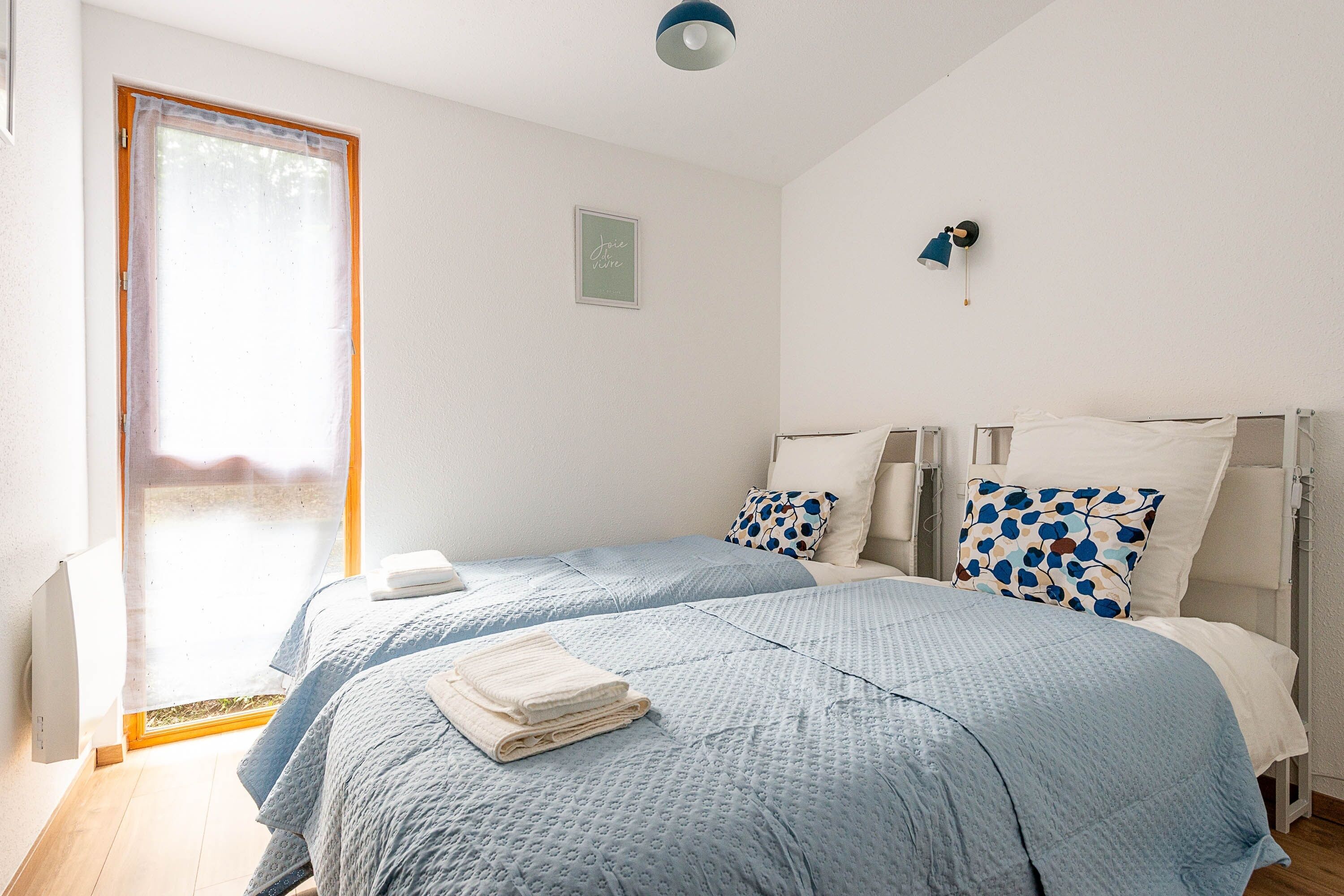 Een slaapkamer met twee bedden, een raam met uitzicht, een bedlampje en een klein, omrande foto aan de muur.