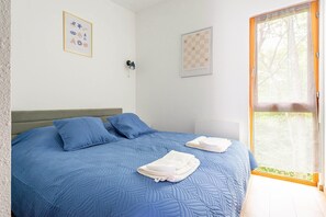 Ein Schlafzimmer mit Bett, Kissen, einem Fenster und Wandbildern.