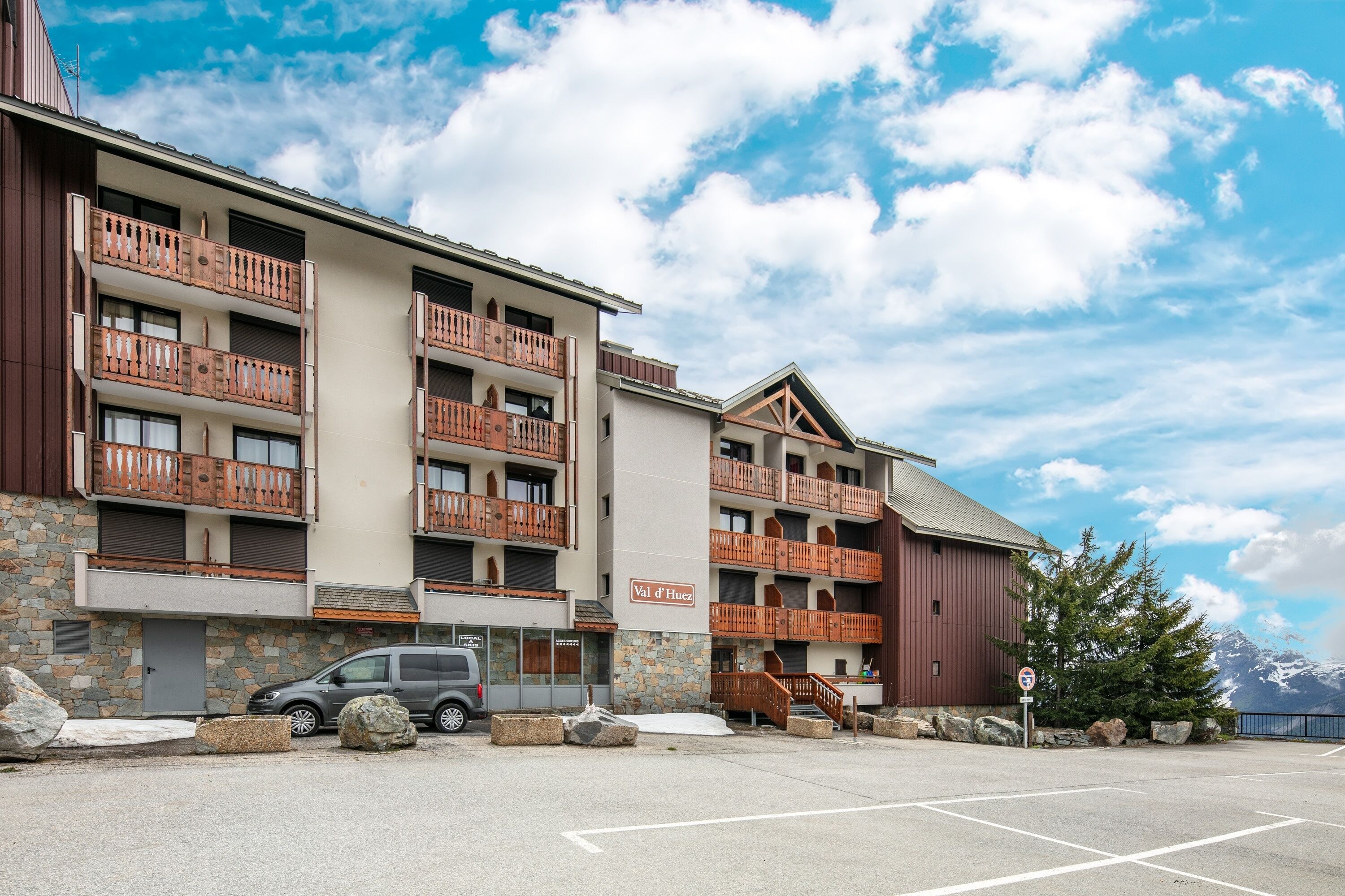 A multi-story hotel with balconies, a stone facade, and a parking area.