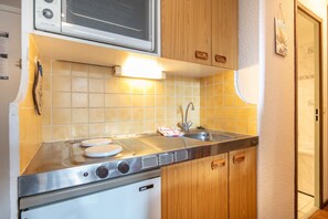 A compact kitchen with a built-in stove, a sink, and wooden cabinets. - CosyPeak Alpe d’Huez - Au pied des pistes (Huez)