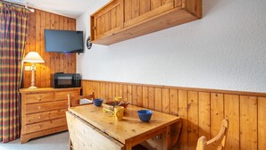 Ein Zimmer mit Holzwänden, einem Holztisch, Stühlen, einem Fernseher, einer Mikrowelle und einer Lampe.