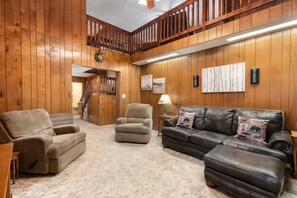 Una sala con paneles de madera, un sofá, sillones, una chimenea y una escalera.