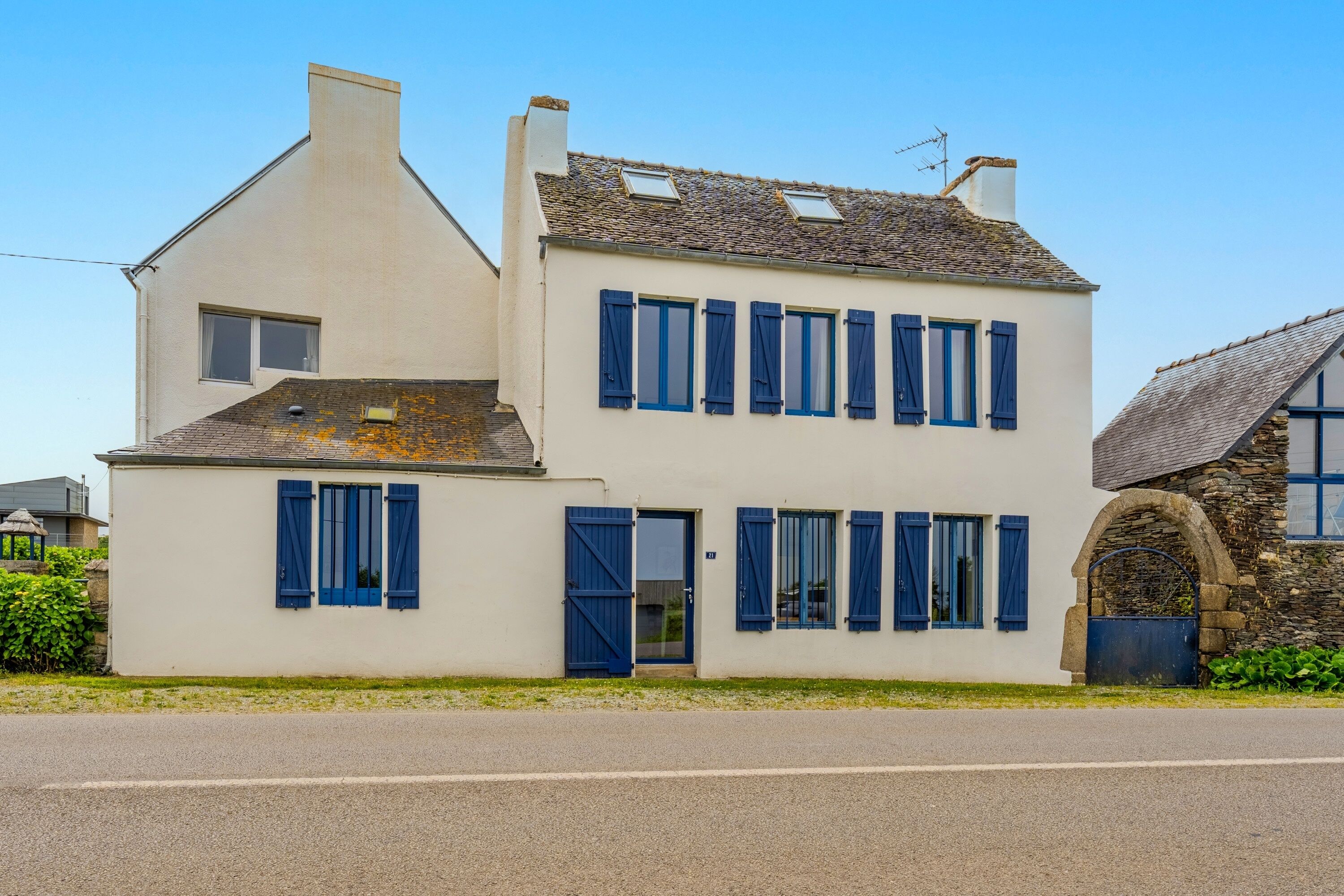 Un bâtiment à deux étages, doté d’une façade blanche et de volets bleus, avec une entrée en arc de pierre et un toit en pente.