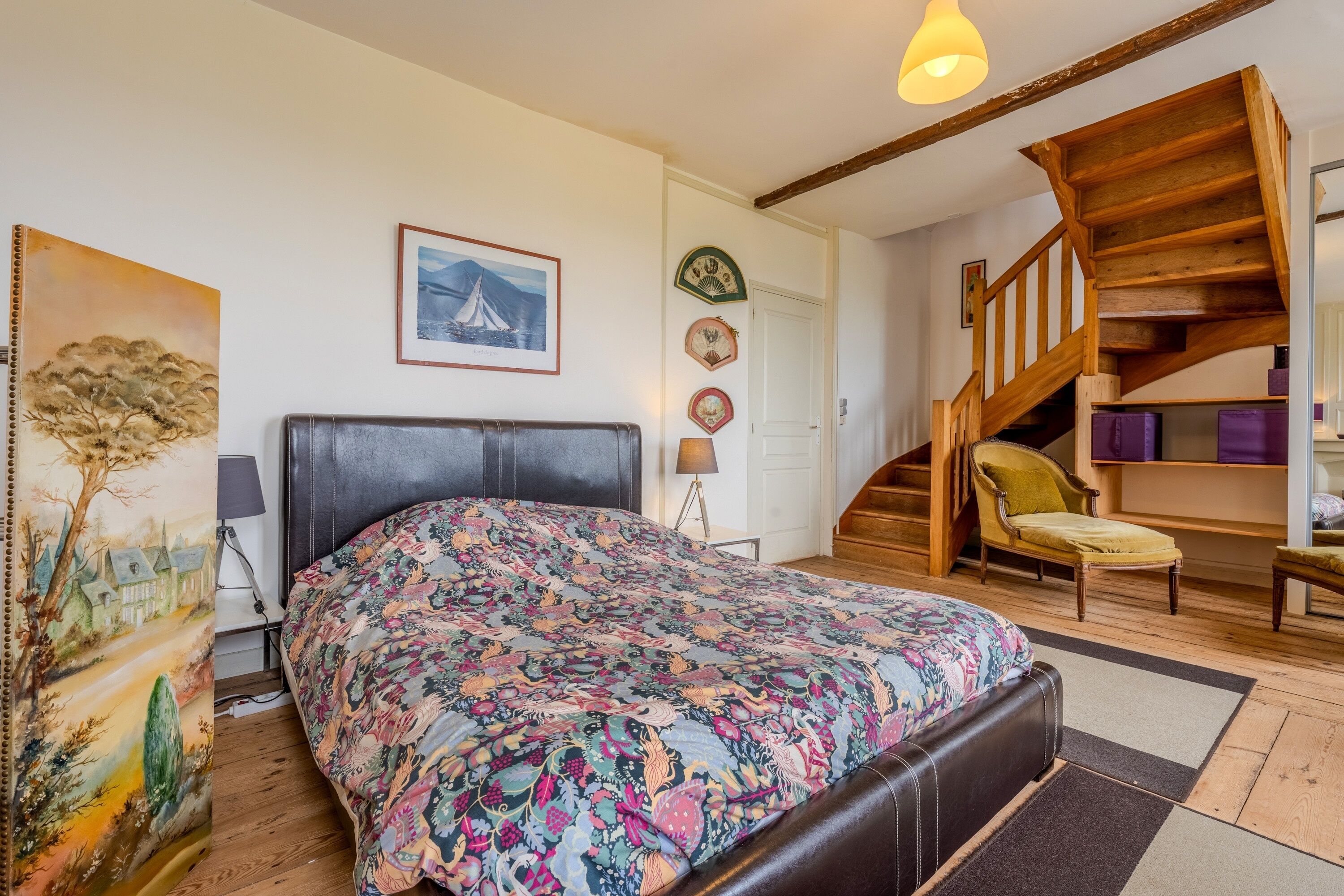 Un dormitorio con una cama, una silla, una escalera y un cuadro en la pared.