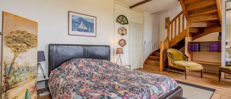 Un dormitorio con una cama, una silla, una escalera y un cuadro en la pared.