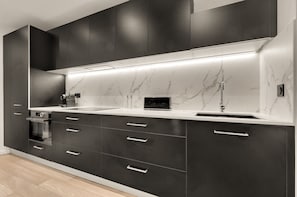 Eine moderne Küche mit dunklen Schränken, einer Marmor-Spritzschutzwand und einem eingebauten Backofen.