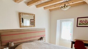 Un dormitorio con una cama grande, un cabecero de madera, una mesita de noche con una lámpara, una silla roja y una ventana con vistas.
