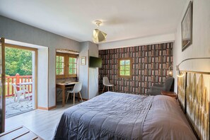 A bedroom with a bed, a desk, two chairs, a bookshelf, and a balcony with a red railing.