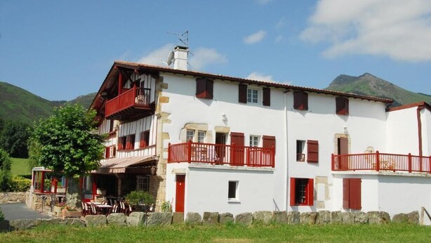 Un edificio de dos pisos con balcones, un muro de piedra y una montaña al fondo.