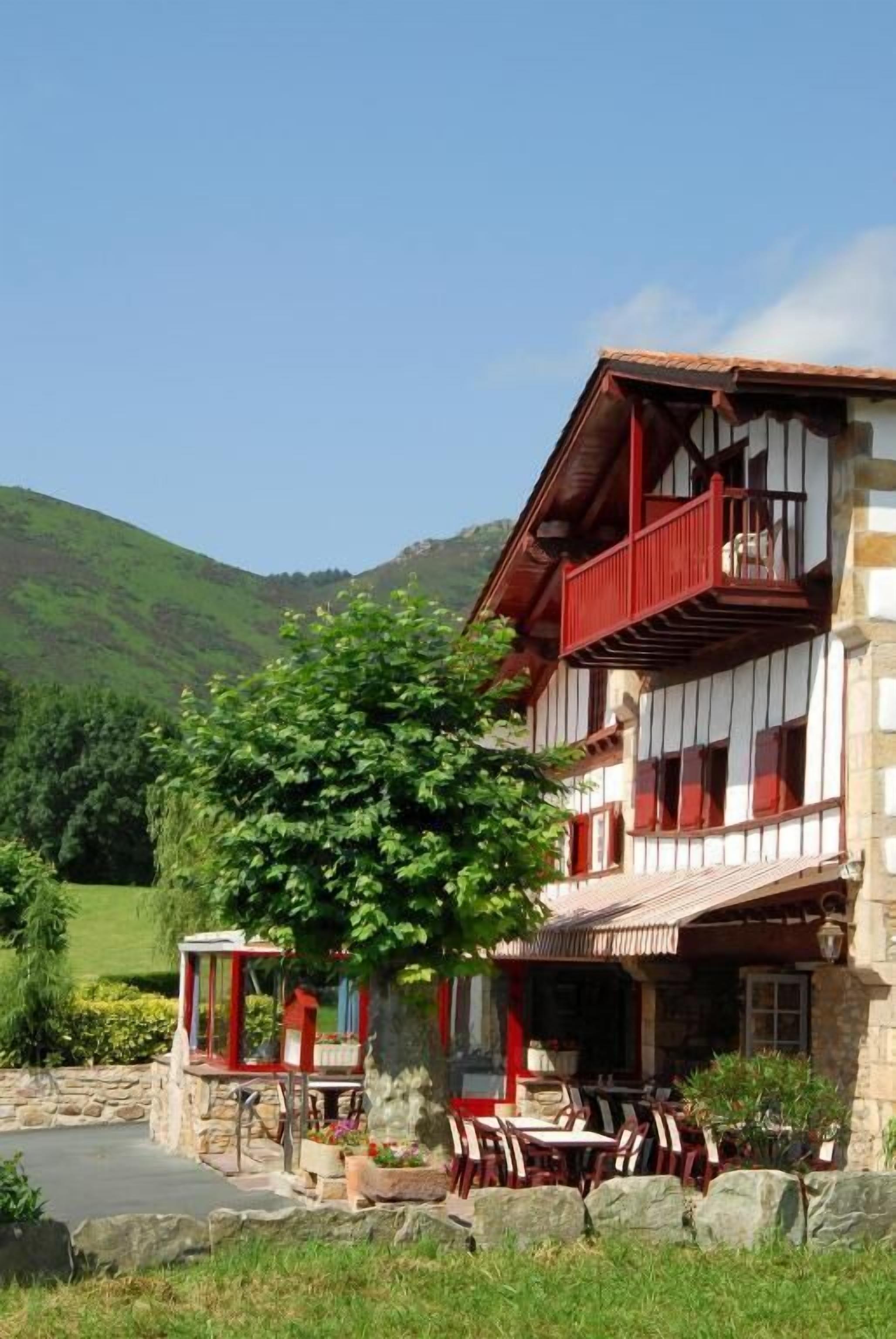 Un bâtiment à deux étages doté d’un balcon, d’un espace extérieur aménagé pour s’asseoir et de fondations en pierre.