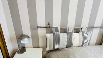 Une chambre avec un lit, une table de chevet avec une lampe, un mur à rayures et un tableau encadré au-dessus du lit.