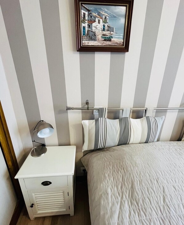 A room with a bed, a nightstand with a lamp, a striped wall, and a framed picture above the bed.
