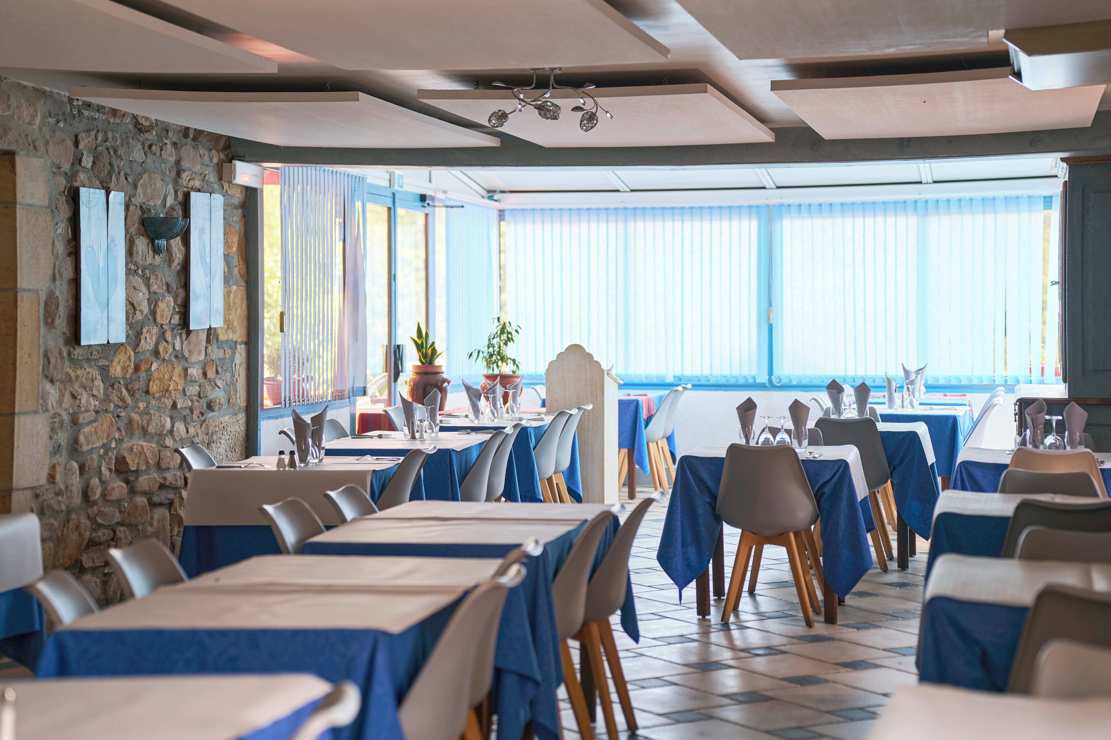 Un restaurante con mesas dispuestas para comer, una pared de piedra y vistas amplias a través de grandes ventanales.