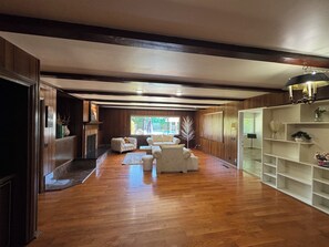 Een ruime kamer met houten vloeren, een open haard en een zithoek met een bank en fauteuils.